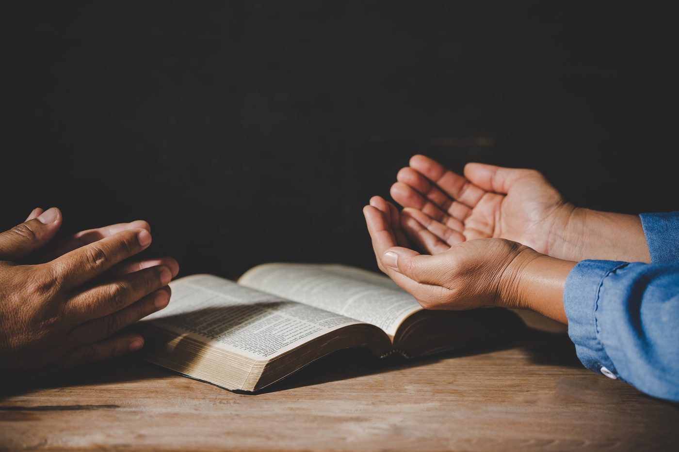 Two people praying with open hands over an open Bible